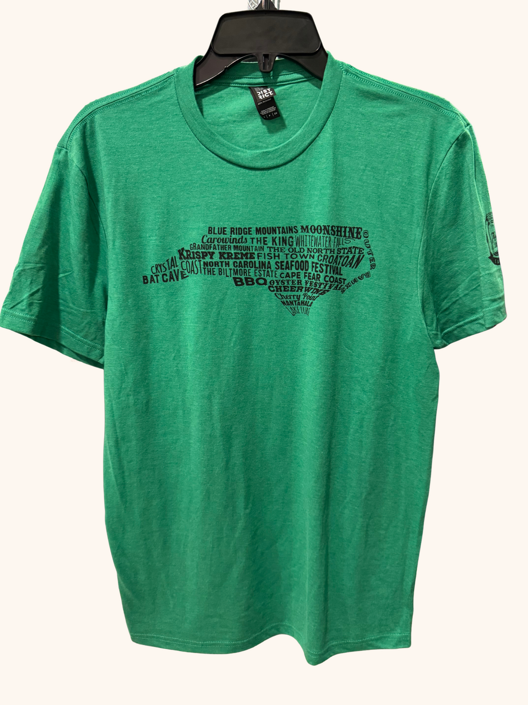 Green t-shirt with black text design on a hanger against a white background