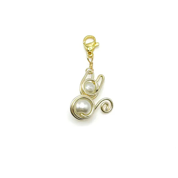 A gold plated wire wrapped around two white Majorca beads in the shape of a cat