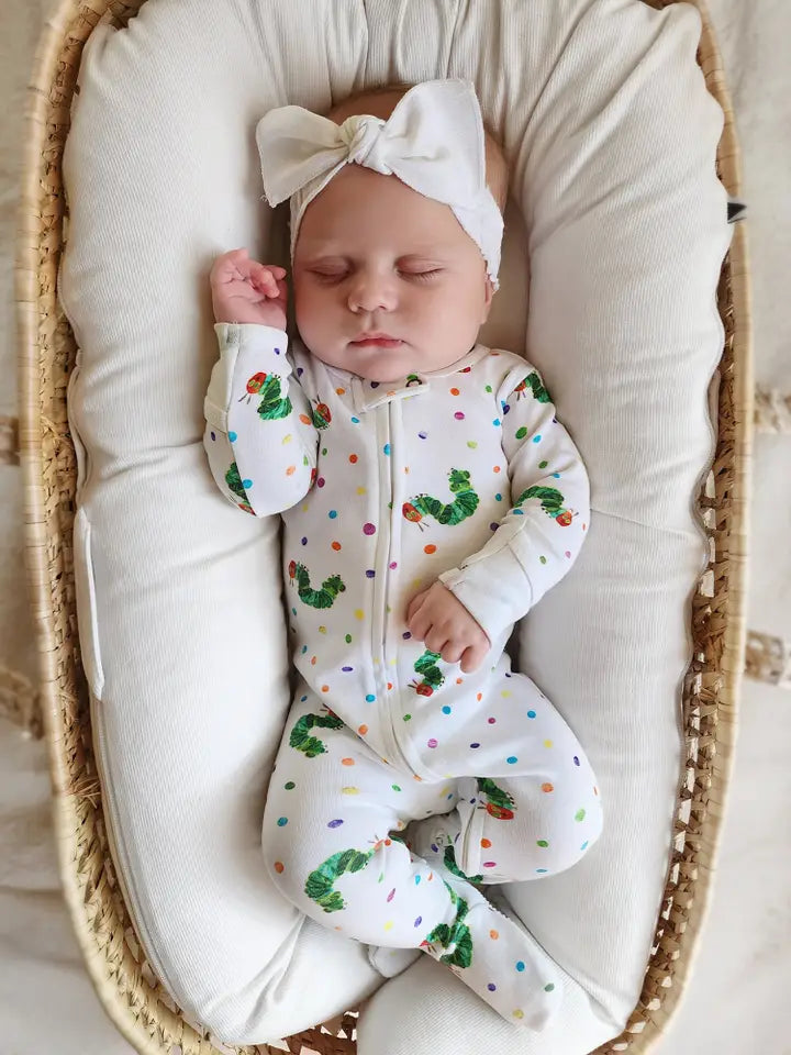 Newborn baby in a white outfit with colorful patterns, sleeping in a moses basket.