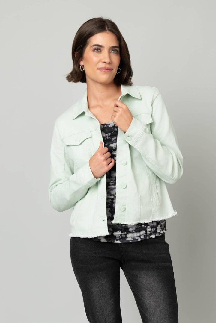 Woman wearing a light green jacket over a patterned top on a gray background