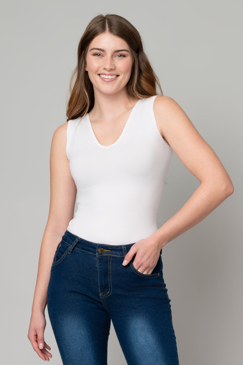 Woman wearing a white sleeveless top and blue jeans against a gray background