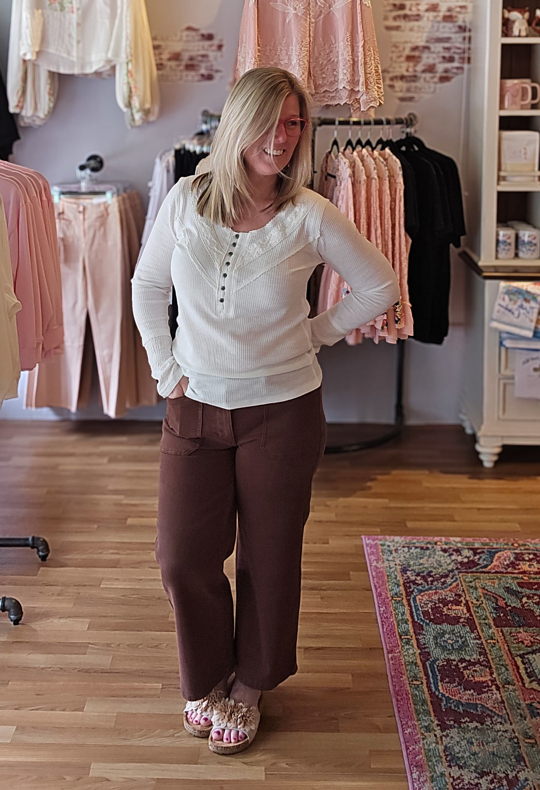 Woman in a clothing store wearing a white top and brown pants.
