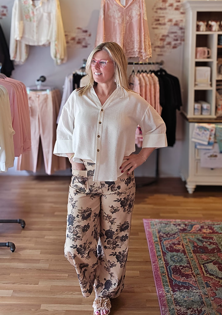 Woman wearing a white blouse and floral pants in a clothing store.