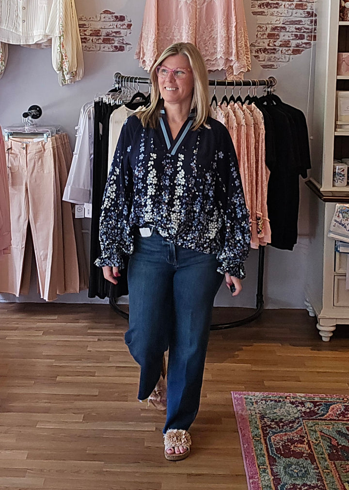 Woman in a floral blouse and blue jeans standing in a clothing store.
