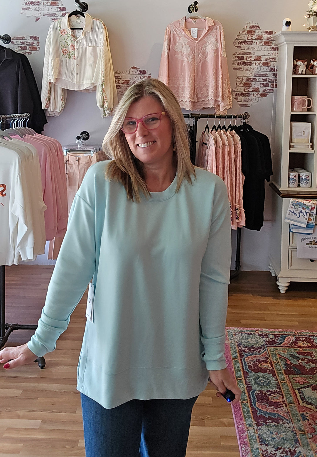 Woman wearing a light blue sweater in a clothing store with racks of clothes in the background.