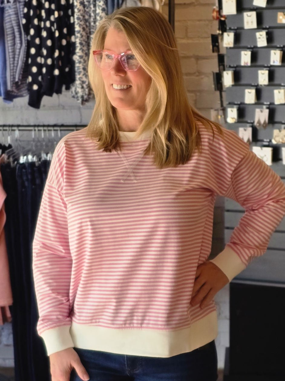 A woman wearing a pink and white striped long-sleeve crewneck sweatshirt, standing in a clothing store.