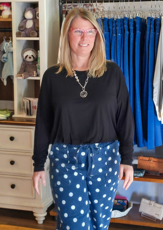 A woman modeling a black long-sleeve top and blue pants with white polka dots in a clothing boutique setting.