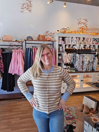 tan and white striped sweater on a woman with blonde hair and pink glasses. Sweater has blue trim on cuffs and neckline. 