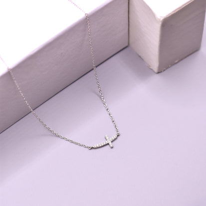 Silver necklace with a small cross pendant on a light gray surface.