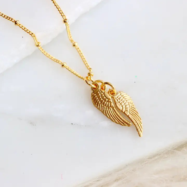 Gold wing-shaped pendant necklace on a marble surface