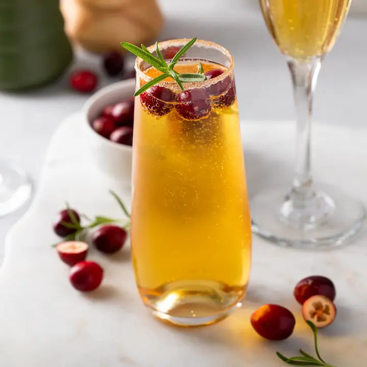 Festive cocktail with cranberries and rosemary garnish on a marble surface.