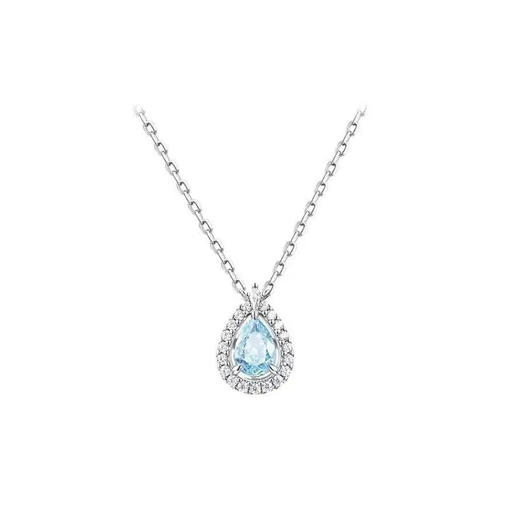 A silver-toned pendant necklace featuring a teardrop-shaped light blue gemstone surrounded by a halo of small clear stones, suspended from a delicate silver chain against a plain white background.