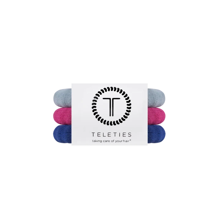Three rolled hair ties in light blue, magenta pink, and navy blue, bundled together with a white paper band featuring the black TELETIES logo and brand name.
