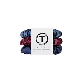 Three satin hair scrunchies in navy blue, burgundy, and dark purple, wrapped with a white paper band featuring the Teleties brand logo.