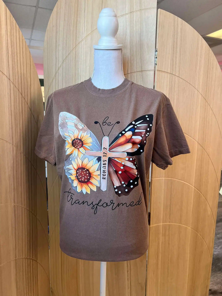 Brown t-shirt with butterfly and sunflower design on a mannequin against a wooden panel background