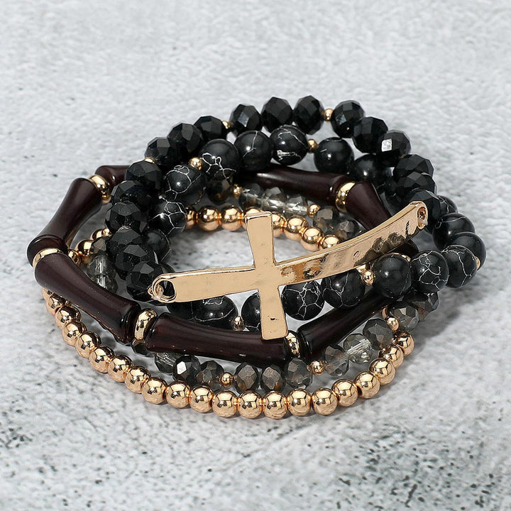 Stack of beaded bracelets with gold crosses on a textured surface