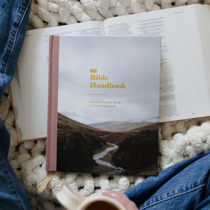 Open book titled 'Bible Handbook' on a textured surface with denim fabric.
