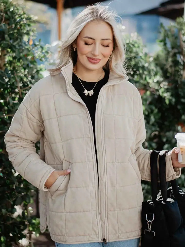 Woman in a beige quilted jacket holding a coffee cup outdoors.