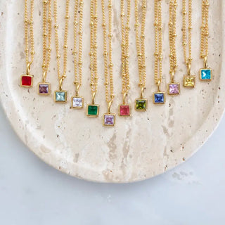 Gold necklaces with colorful gemstones on a textured beige plate.