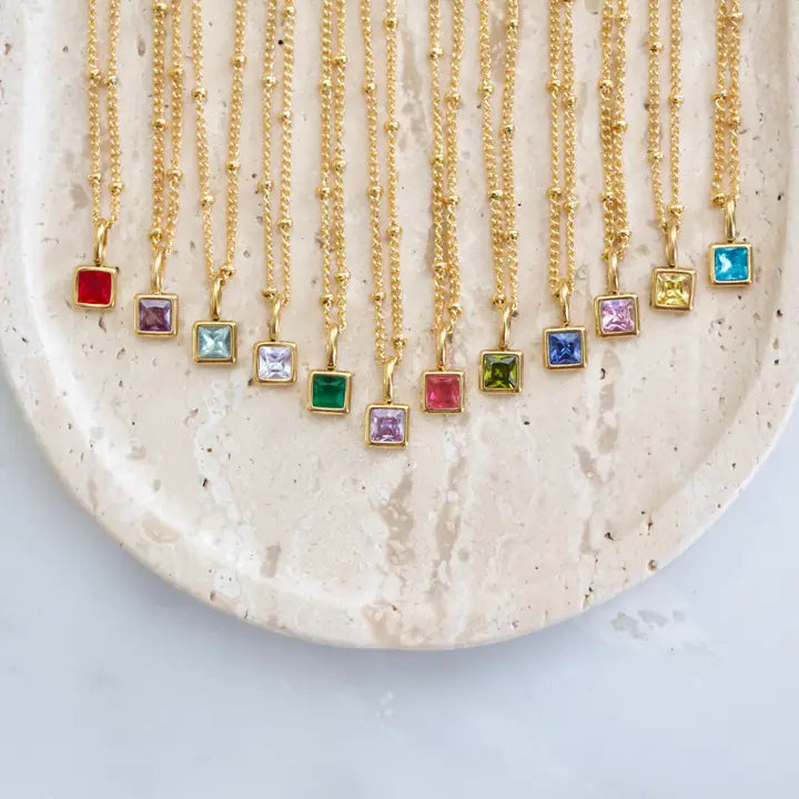Gold necklaces with colorful gemstones on a textured beige plate.