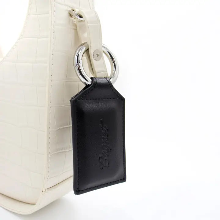 Black leather key fob attached to a white textured bag on a white background