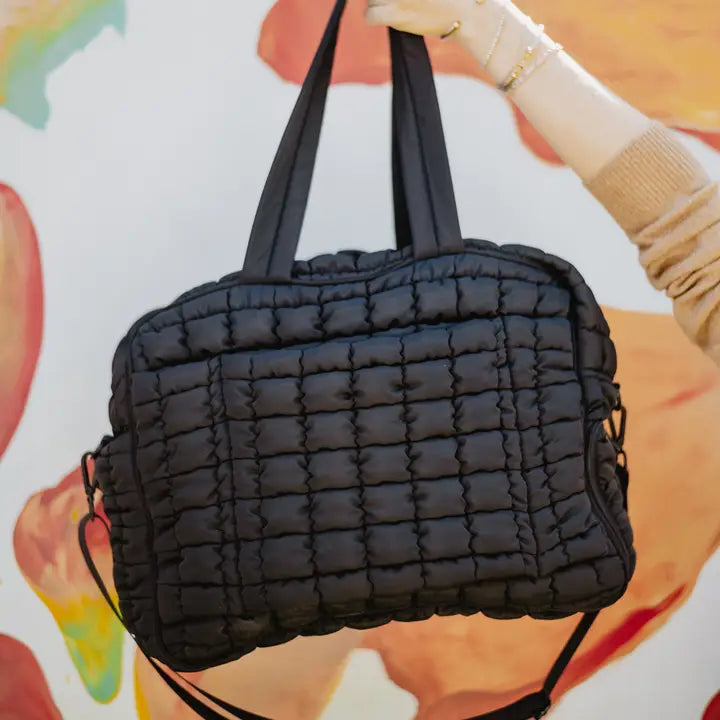 Black quilted handbag held by a person with a colorful background