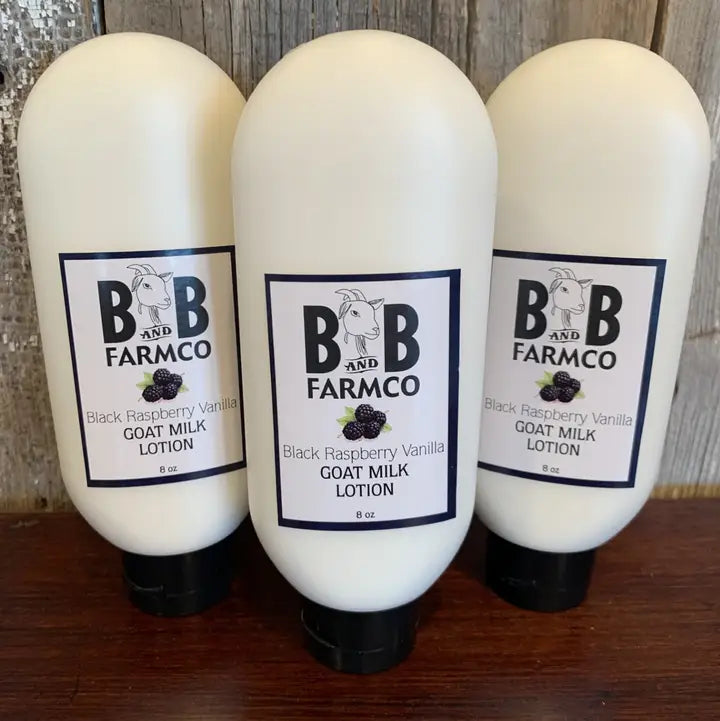 Three white squeeze bottles of BB Farmco Goat Milk Lotion, Black Raspberry Vanilla scent, arranged on a dark wooden surface against a rustic wood plank background.