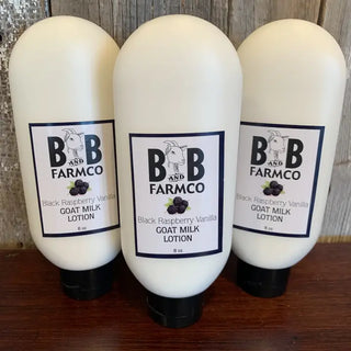 Three white squeeze bottles of BB Farmco Goat Milk Lotion, Black Raspberry Vanilla scent, arranged on a dark wooden surface against a rustic wood plank background.