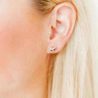 Close-up of an ear wearing a small flower-shaped earring with a blurred background
