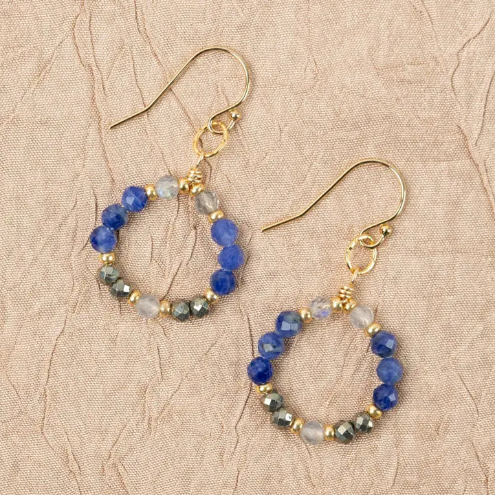 Pair of hoop earrings with blue and gold beads on a beige textured background