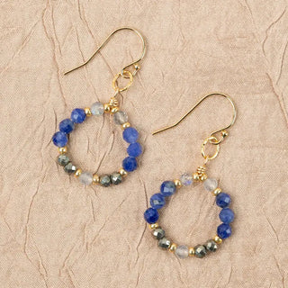 Pair of hoop earrings with blue and gold beads on a beige textured background
