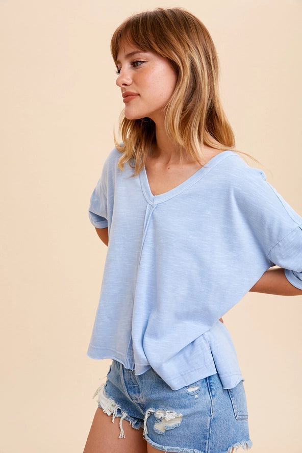 Woman wearing a light blue top and denim shorts against a beige background