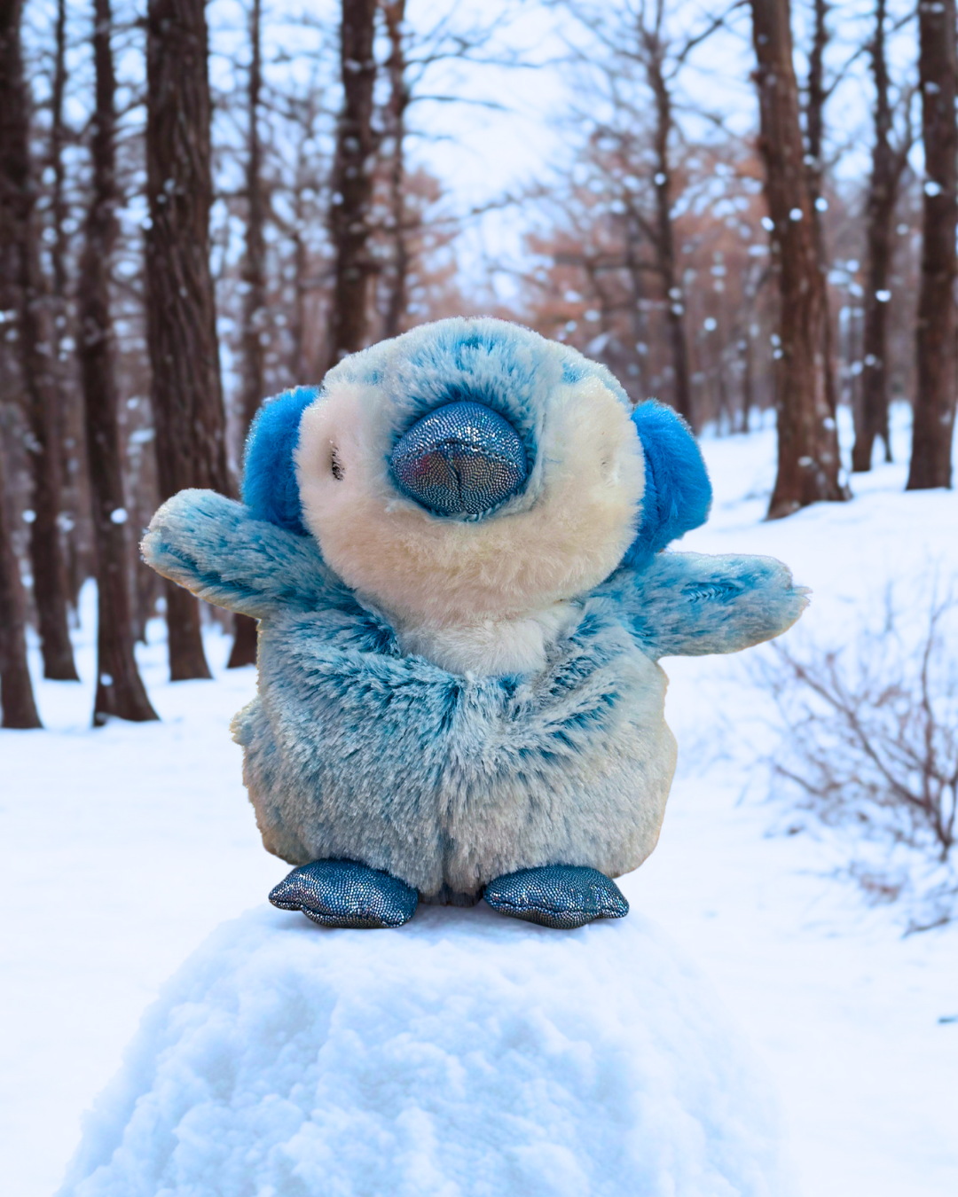 Plush toy resembling a blue creature in a snowy forest