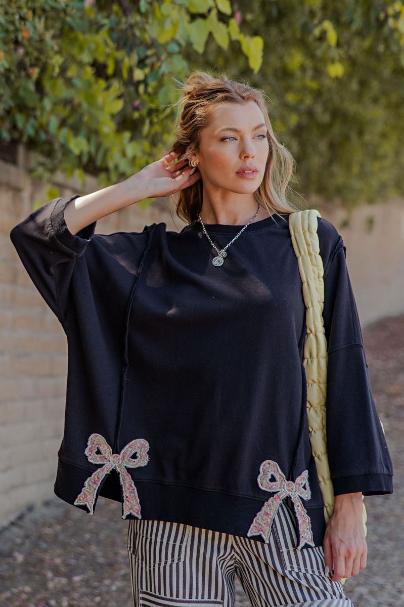 Woman wearing a black oversized sweater with bow details, standing outdoors.