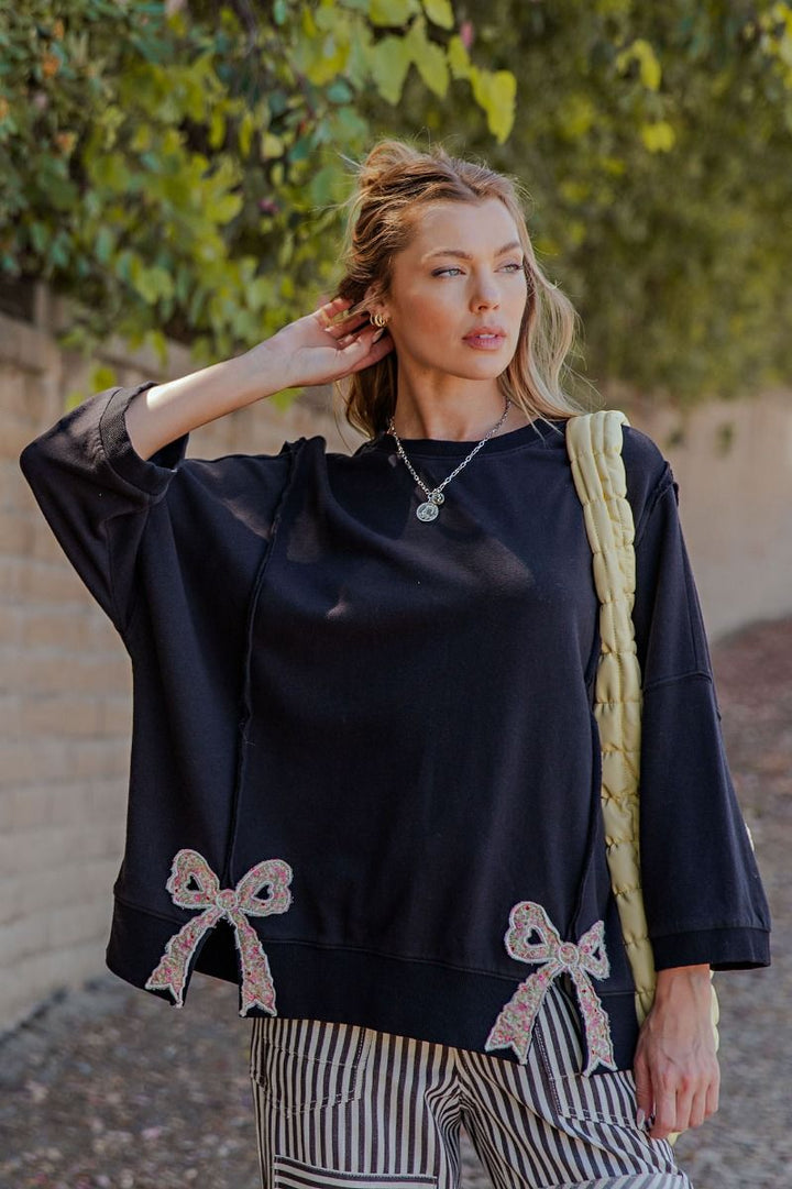 Woman wearing a black oversized sweater with bow details, standing outdoors.