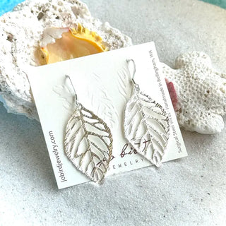 silver leaf shaped earrings with silver hooks on a sandy background