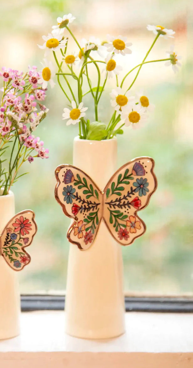 Two small vases with floral arrangements and decorative butterfly wings on a windowsill.