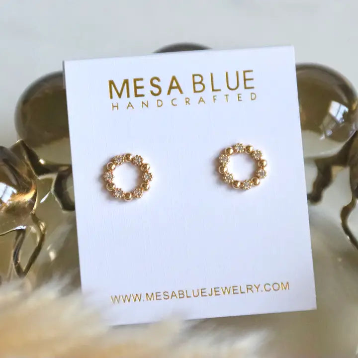 Gold earrings on a Mesa Blue jewelry card with a blurred background