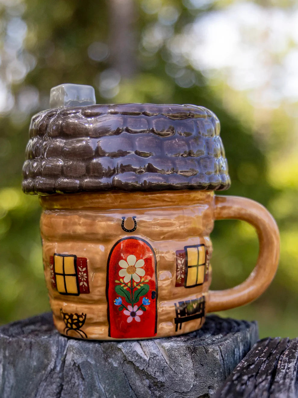 Ceramic mug shaped like a house with a door and windows, outdoors.