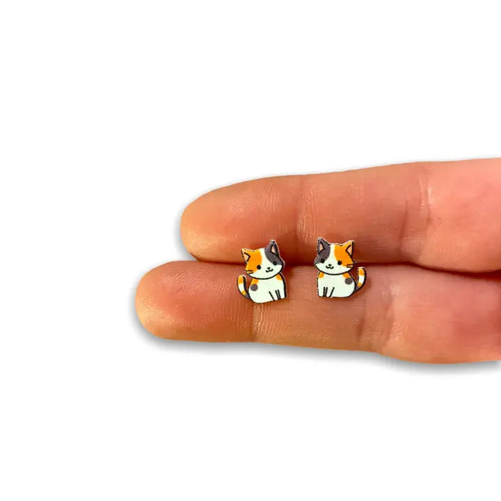 Cat-shaped earrings on a person's finger against a white background