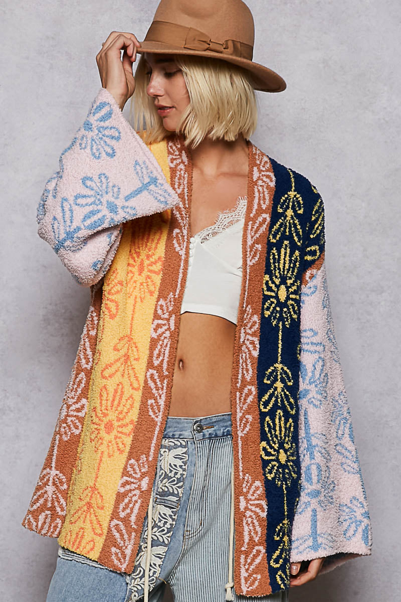 Person wearing a colorful patterned cardigan over a white top and jeans, with a plain background