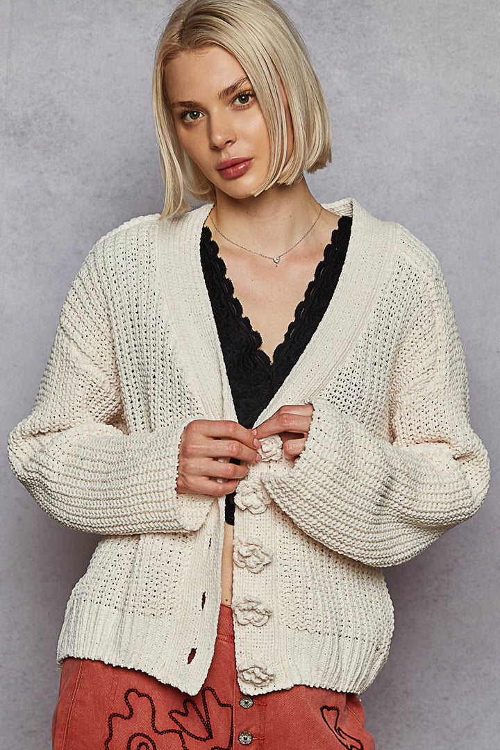 Woman wearing a cream knitted cardigan over a black top against a gray background