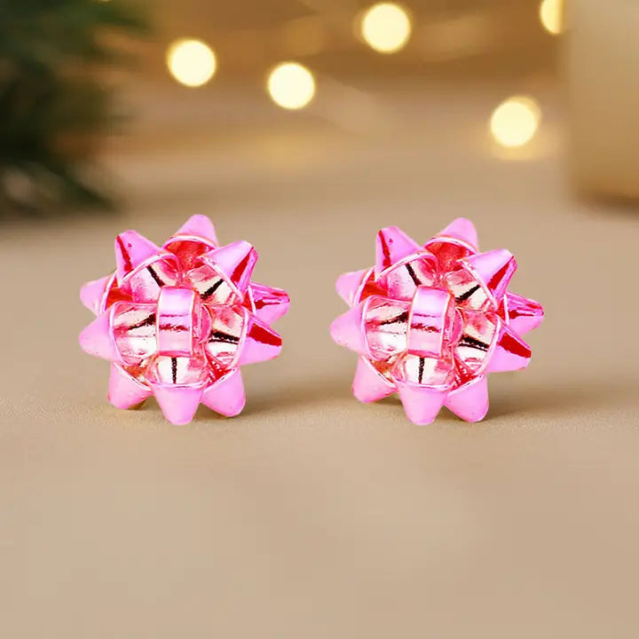 Pair of pink and silver checkered flower earrings on a beige background with blurred lights.