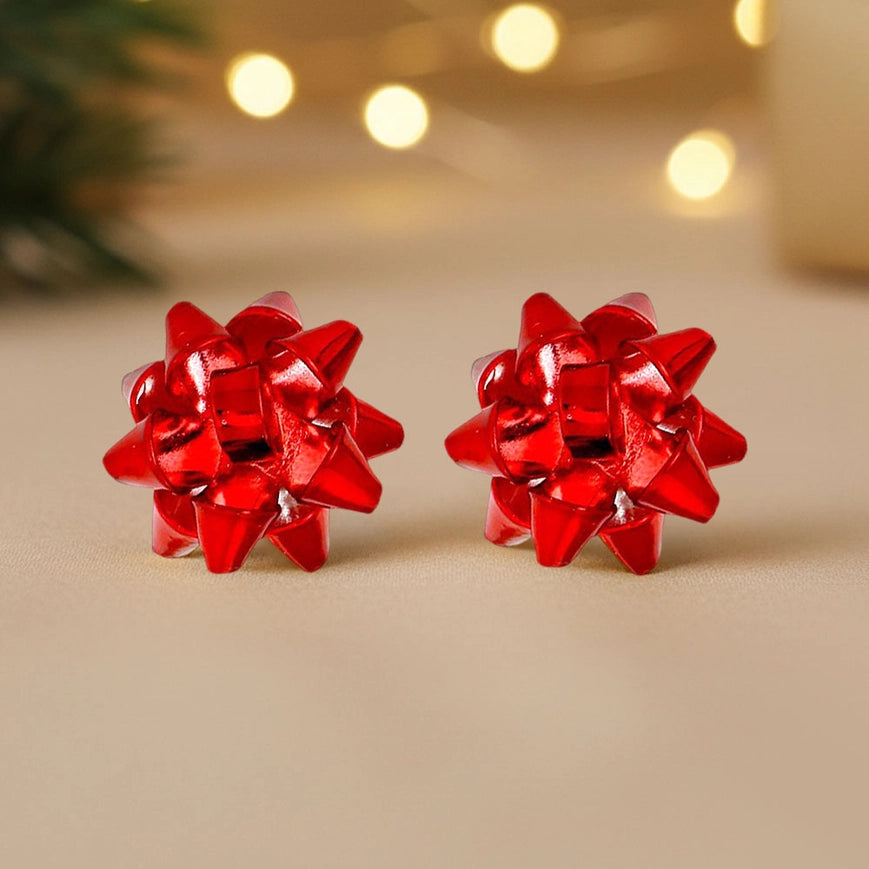 Red bow-shaped earrings on a beige surface with blurred lights in the background