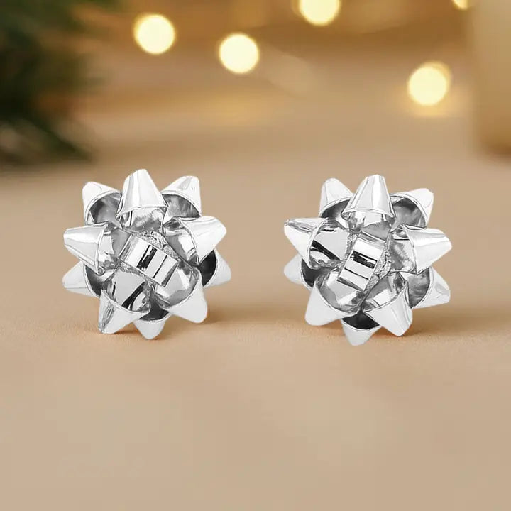 Pair of silver star-shaped earrings on a beige background with blurred lights.