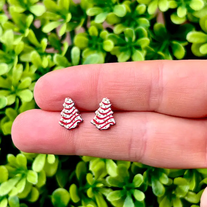 Small red and white striped earrings held between fingers against a green leafy background