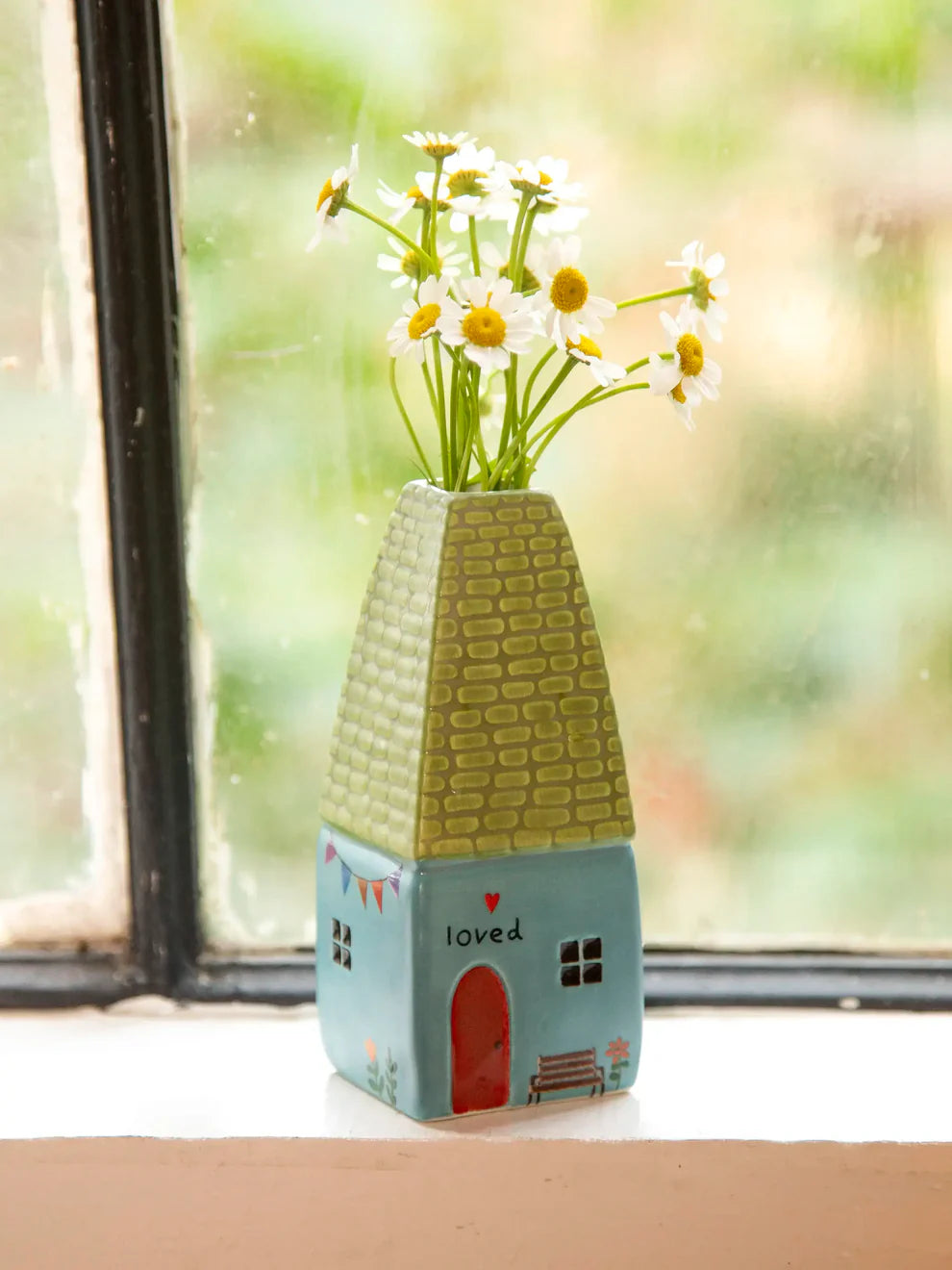 Decorative vase shaped like a house with flowers on a windowsill