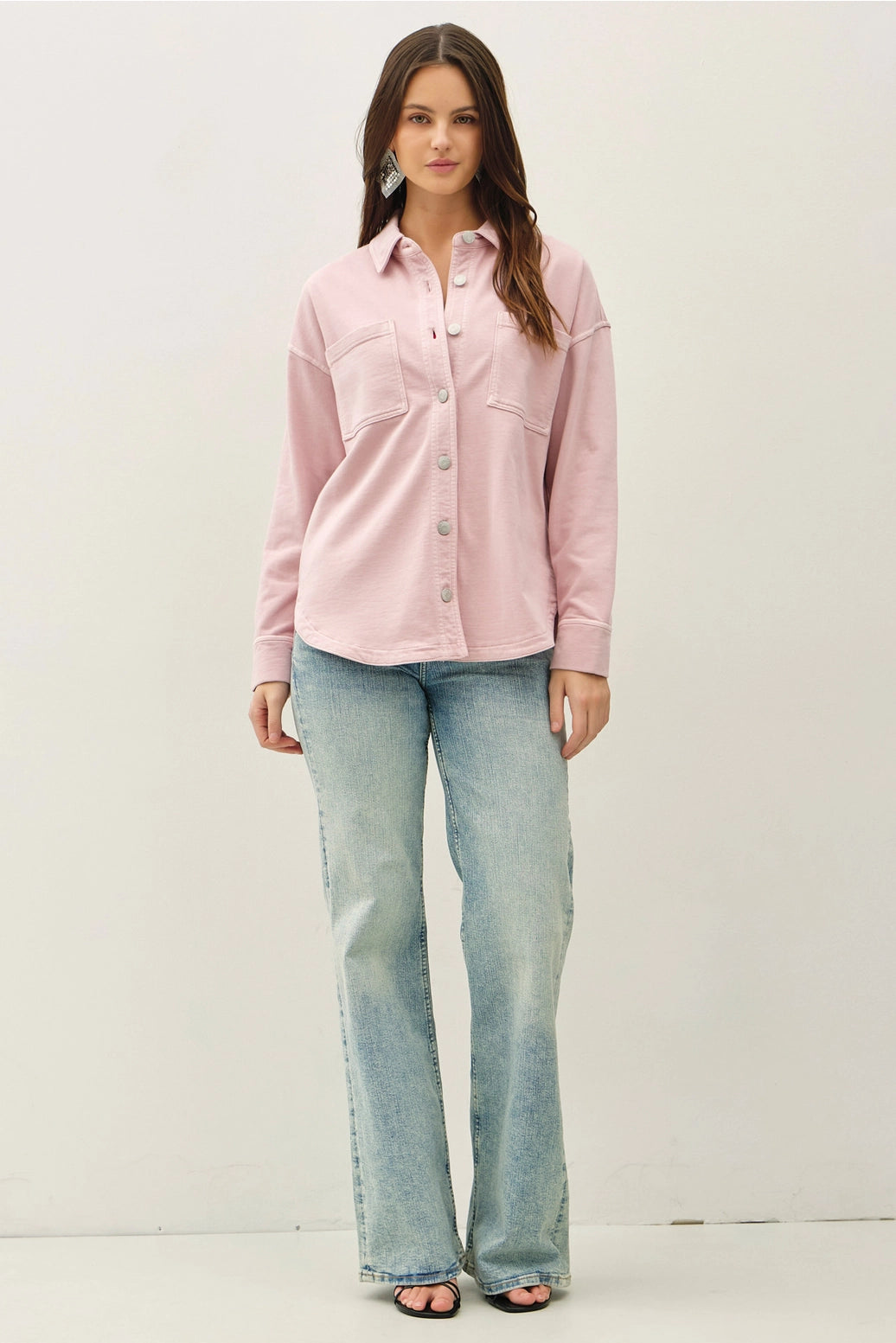 Woman wearing a pink shirt and light blue jeans against a white background