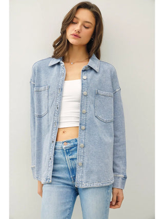 Woman wearing a light blue denim jacket over a white top and blue jeans against a plain background
