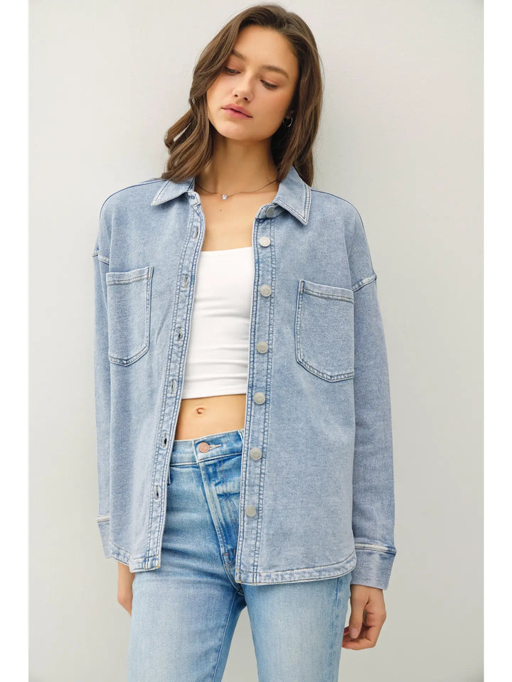 Woman wearing a light blue denim jacket over a white top and blue jeans against a plain background